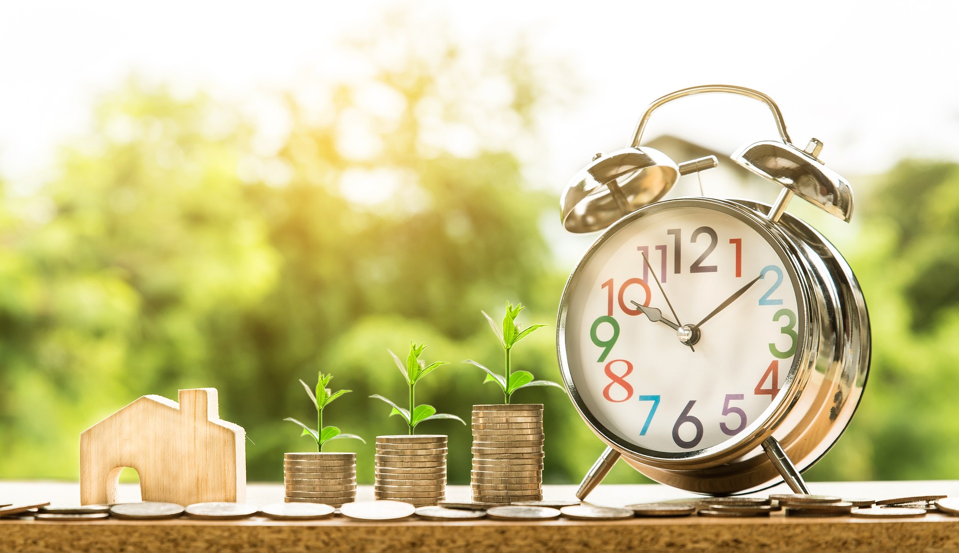 tiny wooden house next to increasing stacks of coins and a clock