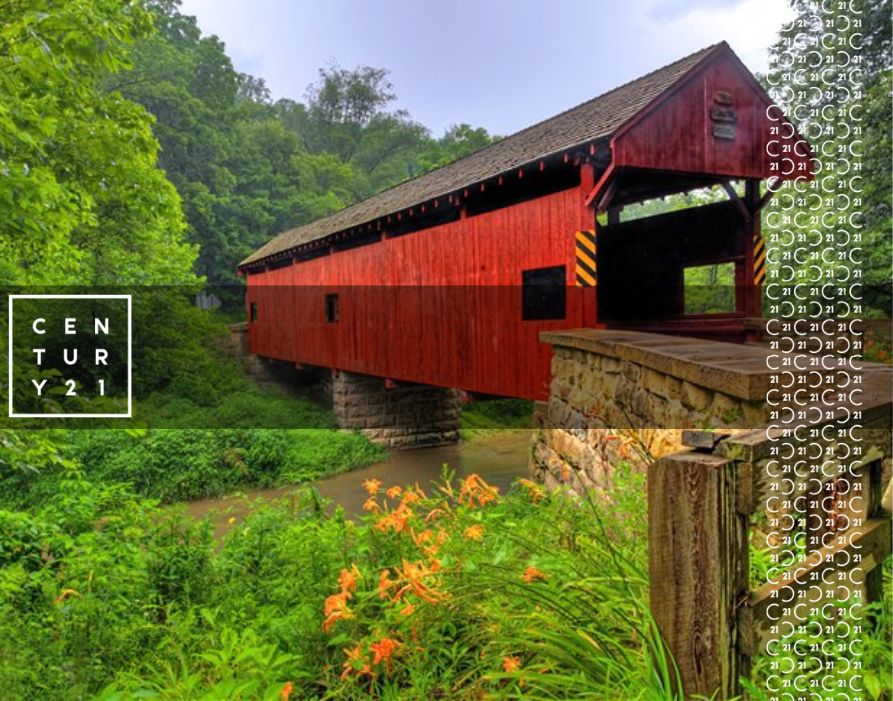 ed covered bridge over a stream with lush green trees, orange wildflowers, and CENTURY 21 branding